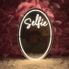 a round mirror with the word selfie written on it in front of some feathers