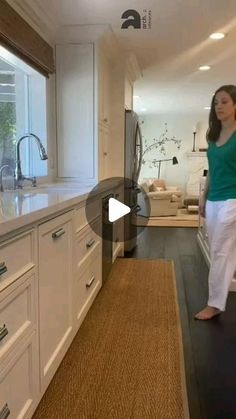 a woman standing in the middle of a kitchen with white cabinets and counter top space