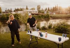 two people standing next to a table with cups on it in front of a body of water