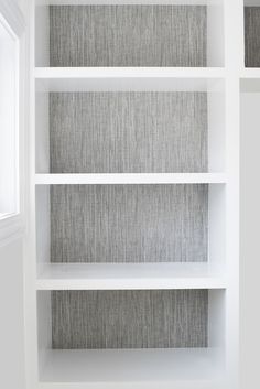 an empty white book shelf with grey linen coverings on the top and bottom shelves