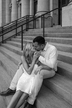 a man and woman sitting on the steps kissing each other in front of some stairs