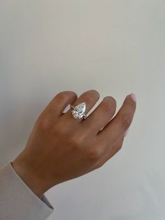 a woman's hand with a diamond ring on her left hand, against a white background