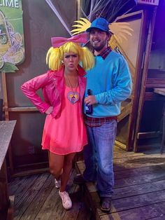 a man standing next to a woman in a pink dress and blue hat on top of a wooden floor