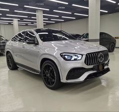 a white mercedes suv is parked in a showroom with other cars behind it and on the floor