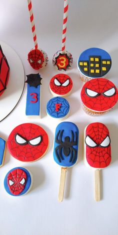 spiderman cupcakes and cake pops are arranged on a white table with candy sticks