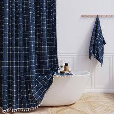 a bath tub sitting next to a blue shower curtain in a bathroom with wooden flooring