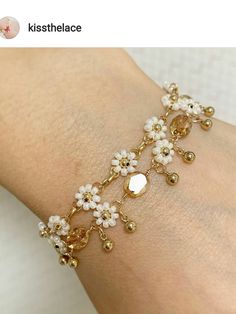 a woman's arm wearing a bracelet with white flowers and gold beads on it