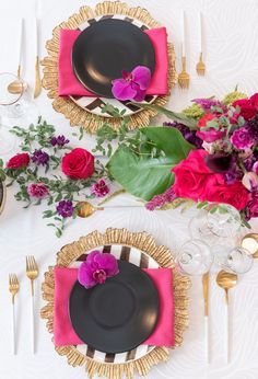 the table is set with black plates, pink napkins and gold place settings for dinner