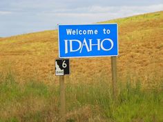 a welcome to idaho sign on the side of a road in front of a grassy hill