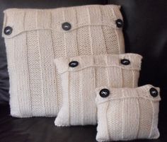 three white knitted pillows sitting on top of a black couch