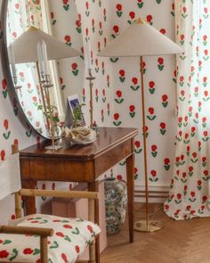 a room with a mirror, chair and lamp on it in front of a flowered wallpaper