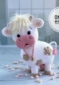 a crocheted cow is standing on the floor with pearls around it's neck