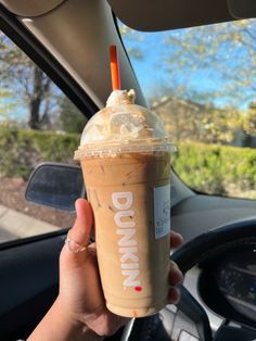 a person holding up a drink in their hand while driving down the road with a steering wheel behind them