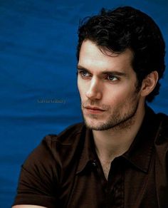 a man with dark hair and blue eyes looks at the camera while wearing a black shirt