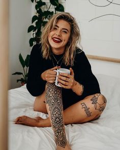 a woman sitting on top of a bed holding a cup and looking at the camera