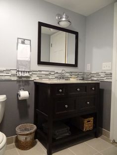 a white toilet sitting next to a sink in a bathroom under a mirror and a wooden cabinet