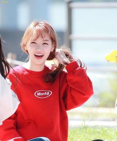 a woman sitting on the ground with her hands behind her head and wearing a red sweater