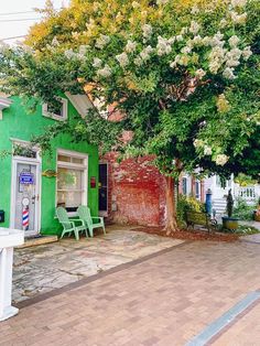 a green building with white flowers on the tree and two chairs in front of it