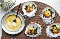 four scallops with sauce and sprinkles on a wooden platter