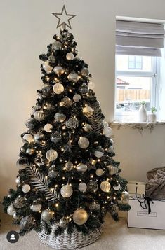 a christmas tree with ornaments and lights in a basket next to a white box on the floor