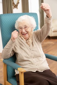 an older woman sitting in a blue chair raising her fist