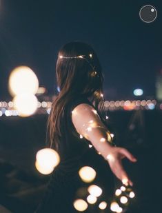 a woman standing on top of a roof at night with her arms out and lights in the air