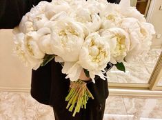 a bouquet of white peonies is held in front of a man's reflection