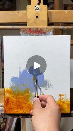 a person is painting on an easel with a paintbrush in their left hand