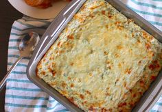 a square casserole dish with cheese and spinach on a blue and white towel