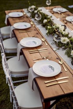 the table is set with white plates and silverware, gold cutlery, greenery and flowers