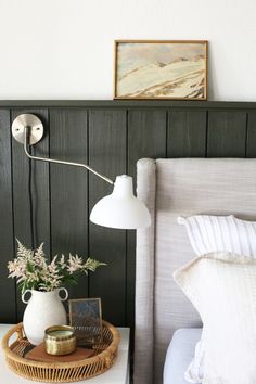 a white lamp sitting on top of a bed next to a basket filled with flowers