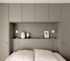 a bed with white sheets and pillows in a room that has built - in shelving