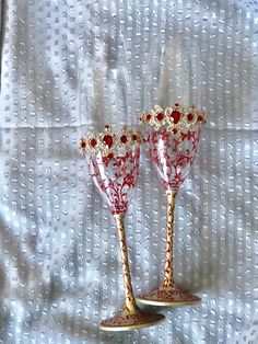 two red and gold wine glasses sitting next to each other on a white tablecloth