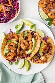 three tacos with shrimp, avocado and cilantro on a blue plate