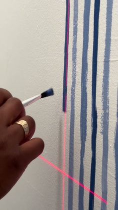 a hand is holding a paintbrush and painting stripes on the wall