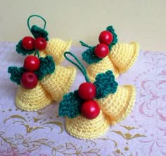 three crocheted bells with cherries on them are sitting on a pink tablecloth