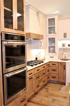 a kitchen with wooden cabinets and stainless steel ovens, white walls and wood flooring