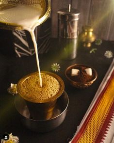 a person pouring milk into a cup on top of a black table next to other items