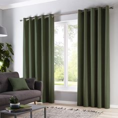 a living room with green curtains and a gray couch in front of a large window