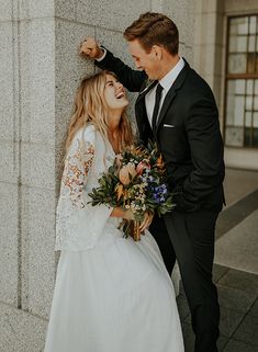 a bride and groom standing next to each other in front of a wall with flowers