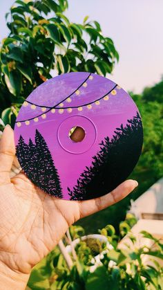 a hand holding up a purple and black object with trees on it's side