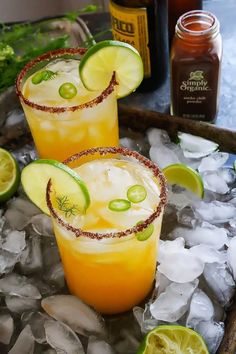 two margaritas sitting on top of an ice tray with lime slices and garnishes