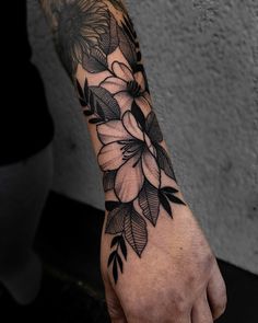 a person with a tattoo on their arm holding onto a hand that has flowers and leaves on it