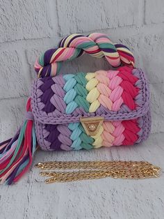 multicolored braided purse with gold chain and tassels on white brick wall