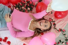 a woman in pink sweater laying on table with balloons and rose petals around her head