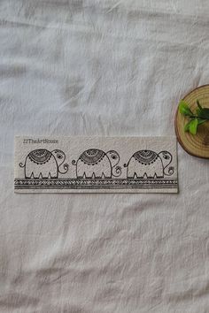 an embroidered cloth with elephants on it next to a straw hat and green leafy plant