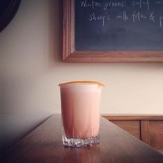 a drink sitting on top of a wooden table next to a chalkboard with writing on it