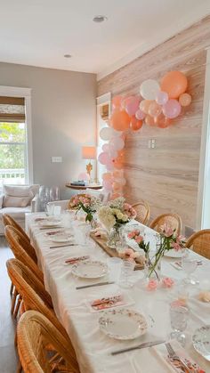 a dining room table set for a party with pink and white balloons hanging from the ceiling