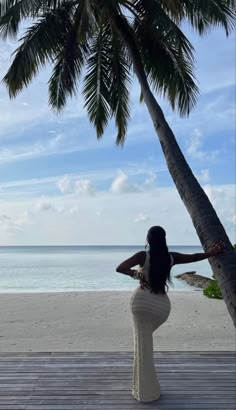 a woman standing on top of a wooden deck next to a palm tree in front of the ocean