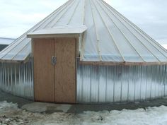 a metal building with a wooden door in the middle of some snow and ice on the ground